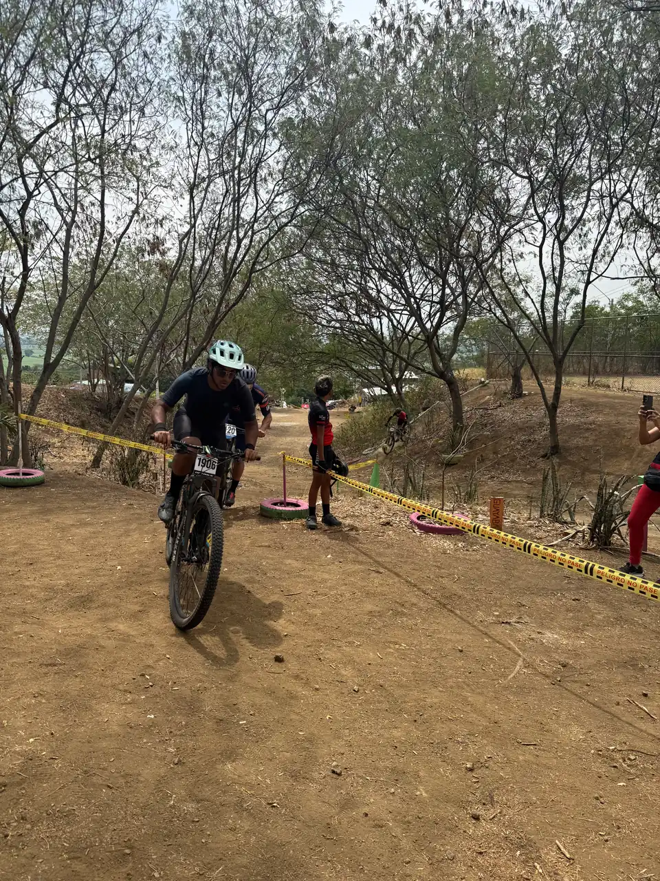 Un corredor de la categoría Open rueda por el circuito junto al letrero de madera que identifica un árbol de guayaba
