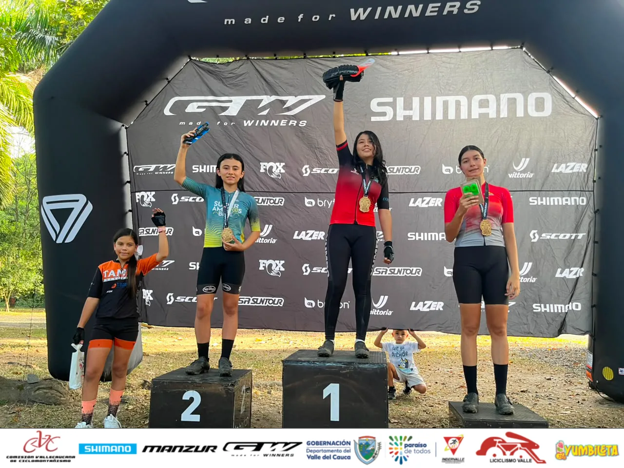 Isabel Quiñones levanta el brazo en el escalón más alto del podio, con la medalla al cuello y una llanta de premio en la mano
